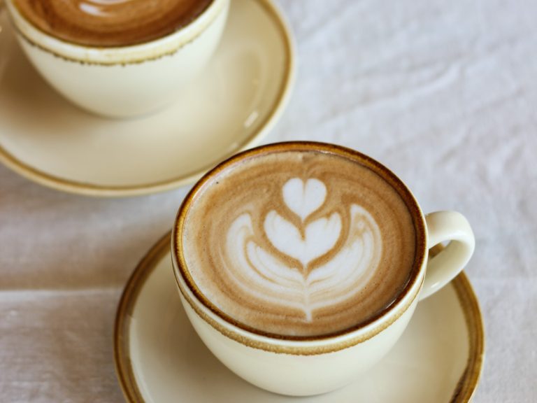 Freshly brewed cup of Waurn Ponds Estate barista-made coffee in a yellow cup and saucer with a flower latte art.