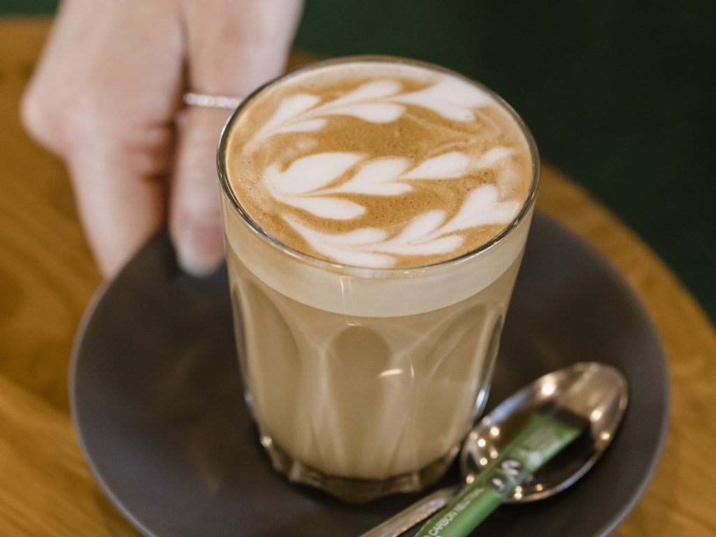 Barista-made latte in a latte glass being served on a black saucer at Waurn Ponds Estate.